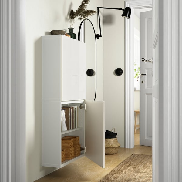 White BESTÅ storage unit with open door revealing books and baskets. Wall-mounted, it saves floor space.