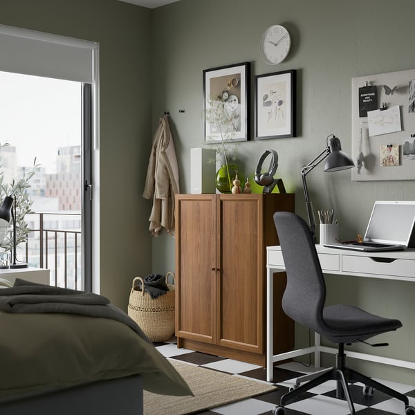 Cosy bedroom with BILLY bookcase, desk, chair, olive-green bed sheets, and green wall with art and clock.