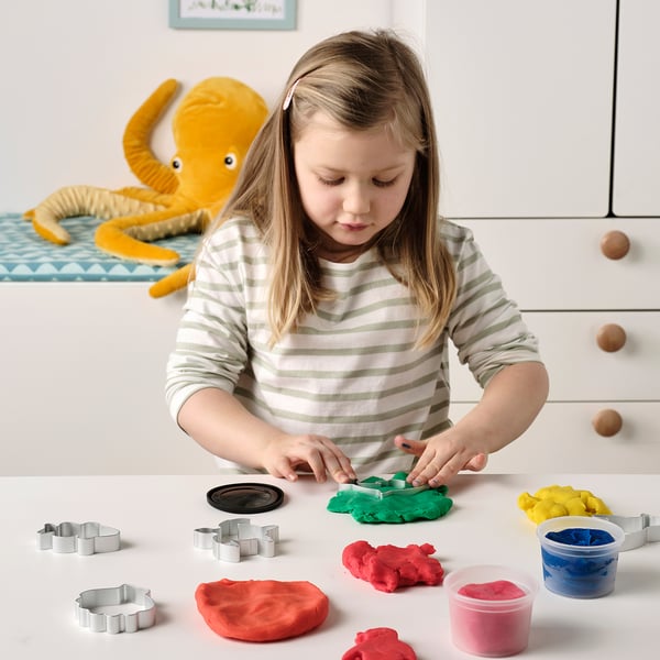 A girl plays with colourful modelling dough and cutters shaped as sea creatures, enhancing fine motor skills and imagination.