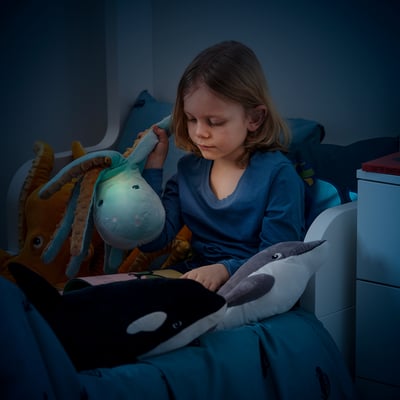 A child reads in bed with a glowing octopus lamp. The lamps head illuminates, providing soft light. The timer ensures it turns off after 15 minutes.
