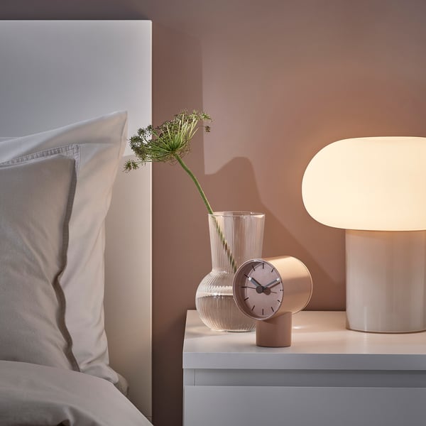 Clock, lamp, and green flowers on bedside table. Alternatively, cosy bedside table with clock, lamp, and green flowers.