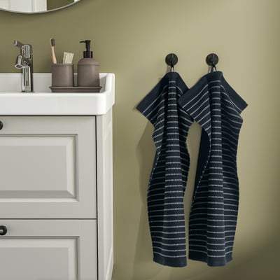 Two blue towels hang on black hooks; white cabinet with silver tap.