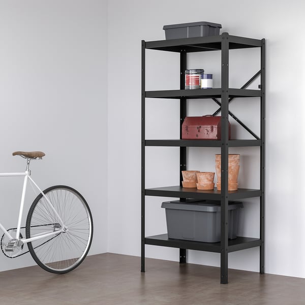 BROR: black metal shelf stands tall near white bike; holds grey bins, red box, clay vases. Durable, flexible.