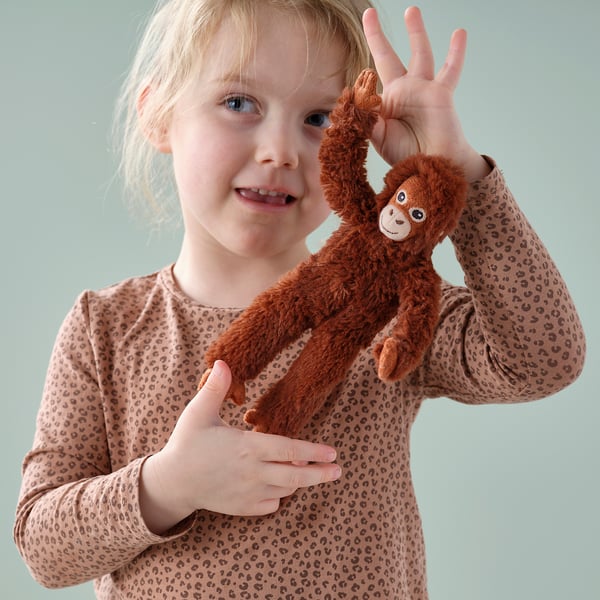 Child holding plush orange monkey toy; monkeys arms raised, child smiling.