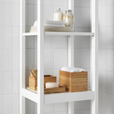 White bathroom shelves holding neatly stacked towels and bamboo boxes, one containing cotton wool.