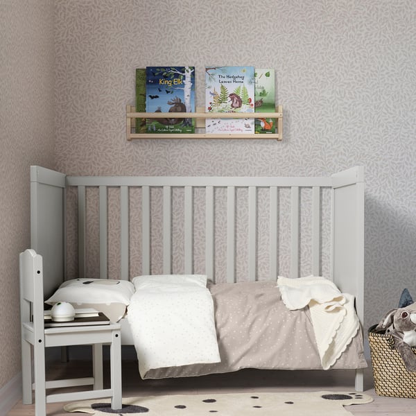 Childs room with DRÖMSLOTT rug, white crib, wall shelf with books. Soft, grey rug fits under crib.