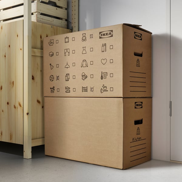 Stacked ikea boxes with household icons, DUNDERGUBBE, beside cabinet.