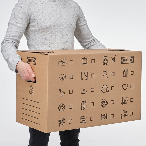 Person holding large cardboard moving box labelled IKEA with various icons, designed for easy lifting and carrying, stacking, and recycling.