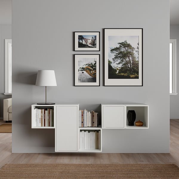 Modern living room with grey wall featuring white storage unit holding books and a lamp, topped with three framed nature photos.