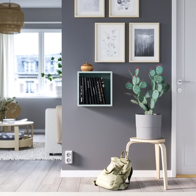 Modern room with EKET storage, records, plant. Backpack under cactus, stool, art, city view.