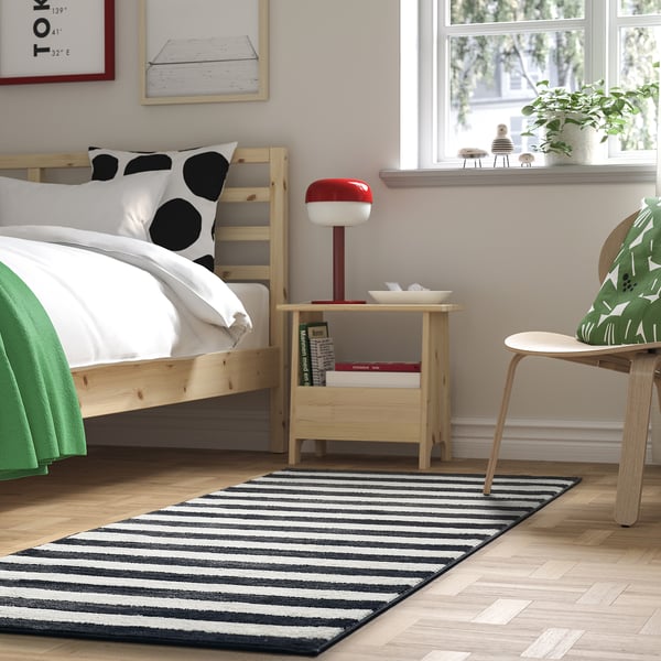 Bedroom with polka dot bed, wooden bedside table, and black/white striped rug.