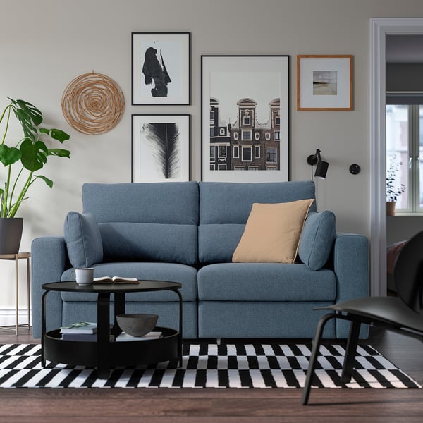 Blue ESKILSTUNA sofa in cosy living room with adjustable headrests, coffee table, side table, and gallery wall.