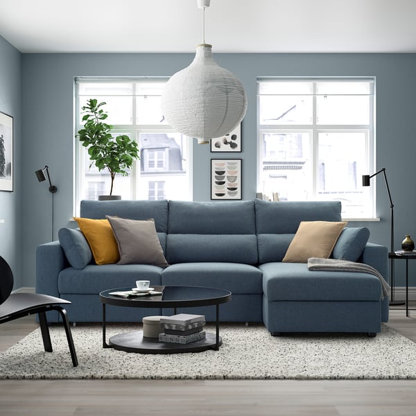A cosy living room with a blue ESKILSTUNA sectional sofa, high backs, adjustable headrests, and a matching ottoman.