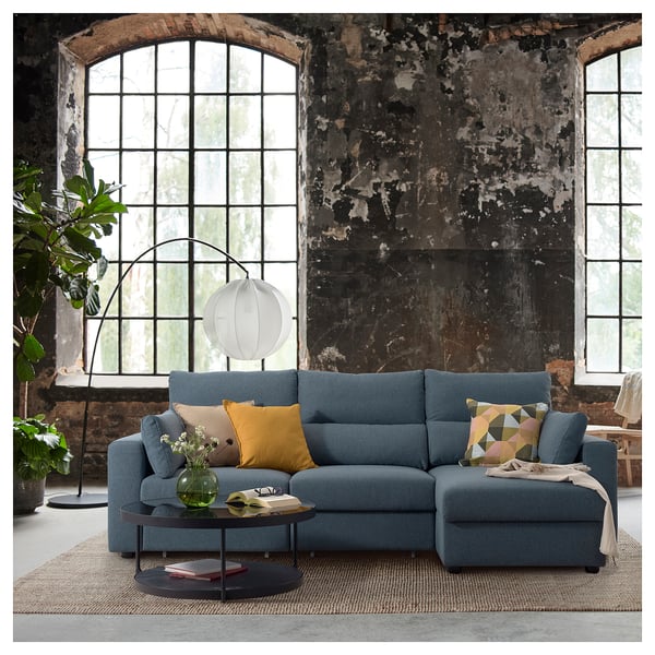 Modern living room with blue sectional sofa, colourful pillows, round coffee table, large windows, and floor lamp.