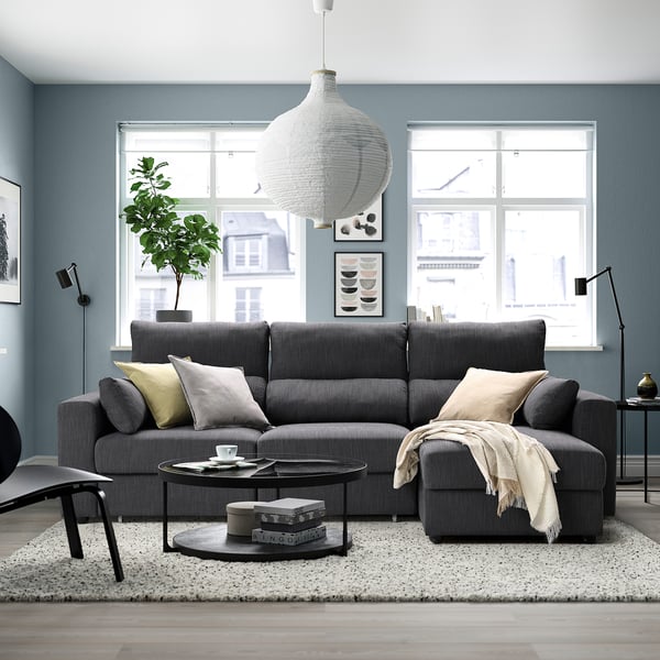 Modern living room with grey sectional sofa, adjustable headrests, and a pendant lamp above. Large window brings in natural light.