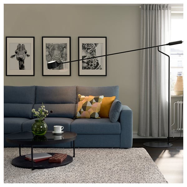 Modern living room with blue sofa, colourful pillows, glass coffee table, green vase, artwork, floor lamp.