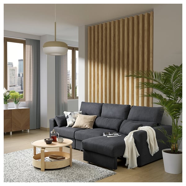 Modern living room with grey ESKILSTUNA sofa, wooden coffee table, large plant, and city view.