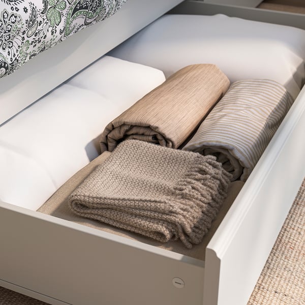 Open white bed drawer with neatly folded blankets and towels inside.