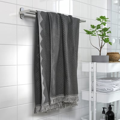 Bohemian-style bath towel in grey hangs near plant and neatly folded towels on white shelving.