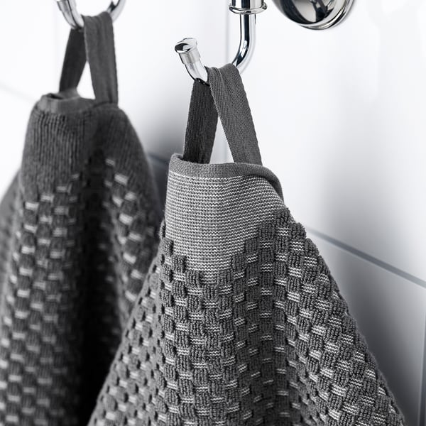 Two towels hang neatly on hooks, one woven with a patterned front and plain back, practical for use in a bathroom.