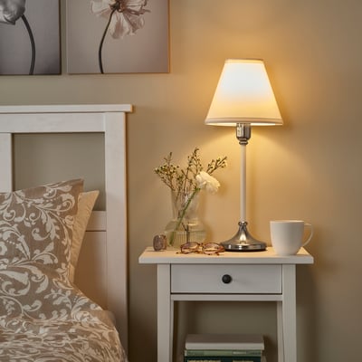 Bedside table with FLYGHÖJD lamp, warm light, vase, mug, glasses