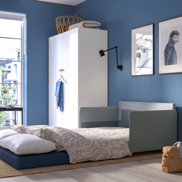 Modern, compact sofa-bed in small room. Blue wall, white cabinet, cat art. Easy convertible for sleep.