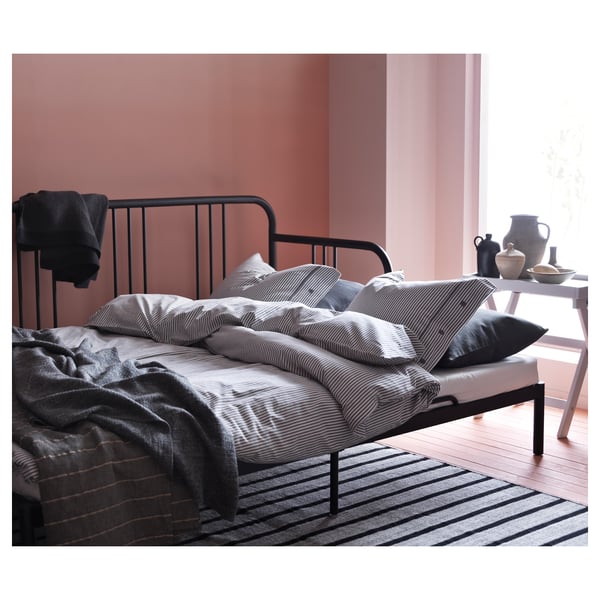 Modern black metal day-bed with striped linens in a cosy bedroom.