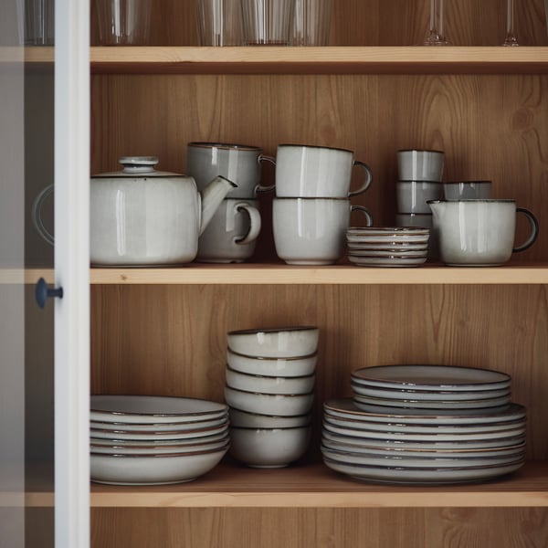 Wooden shelves with GLADELIG stoneware plates, bowls, cups, and teapot, clean shapes.