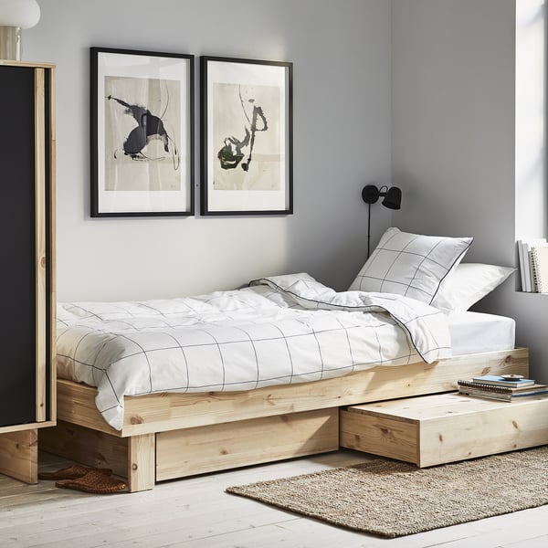 Minimalist bedroom with a GLAMBERGET wooden bed, featuring white bedding and abstract wall art.
