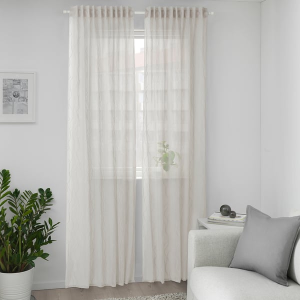 Grey GLESGRÖE curtains with wave pattern softly hang, allowing light and creating cosy atmosphere. Nearby plant and sofa with pillow are smaller.