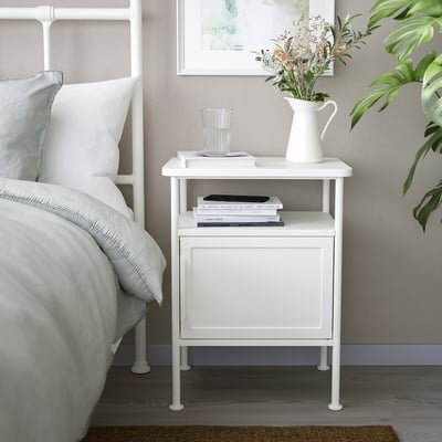 GRÅFJÄLLET bedside table in white with shelves and cabinet. Holds books, a glass, and a vase. Soft industrial design fits next to bed.