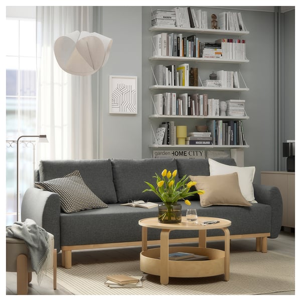 Modern living room with grey GRUNNARP sofa-bed, wooden coffee table, and white bookshelves filled with books.