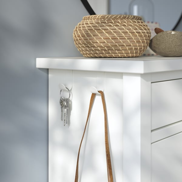 White GULLABERG shoe cabinet with 2 hooks holding keys and a strap. Woven basket and decorative rock on top, grey wall behind.