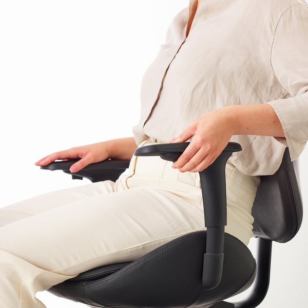 Person adjusting office chair armrest. The HATTEFJÄLL chair offers 2d adjustable armrests, a key ergonomic feature for comfort and posture support.