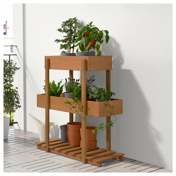 Brown wooden 3-tier plant stand with various potted plants against a white wall.