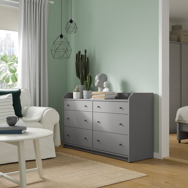 Modern living room with grey HAUGA chest of drawers, white armchair, coffee table, and large window with curtains.