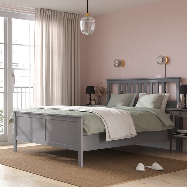 Modern bedroom with grey HEMNES bed, pink walls, wooden floor, pendant lamp, and slippers.
