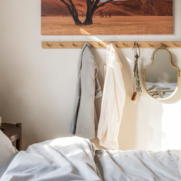 Bedroom with white bed, oak coat rack, grey and white towels, gold mirror, desert art.