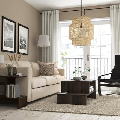 Minimalist living room with beige sofa, wooden coffee table, black armchair, large window, and pendant lamp. Beige walls and neutral rug.