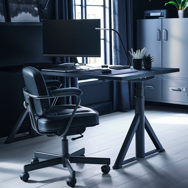 Modern home office setup with black IDÅSEN desk, ergonomic chair, and large monitor.