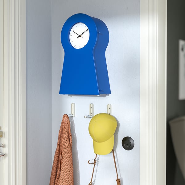 A blue wall clock hangs above hooks with a hat and towel.