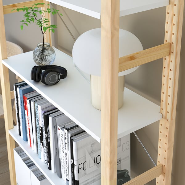 A modern bookshelf with wooden frame holds books, headphones, and a small plant.