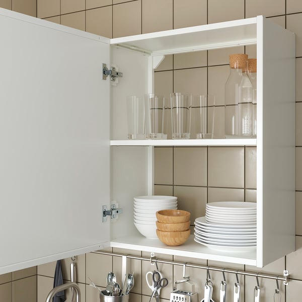 White kitchen cabinet with glassware, plates, bowls, and hanging utensils.