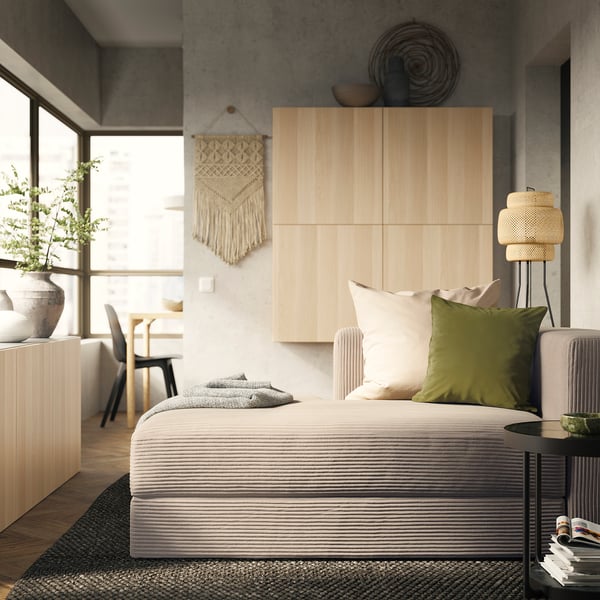 Modern bedroom featuring JÄTTEBO sofa with neutral tones, wooden panels, and a macrame wall hanging, offering a cosy and minimalist aesthetic.