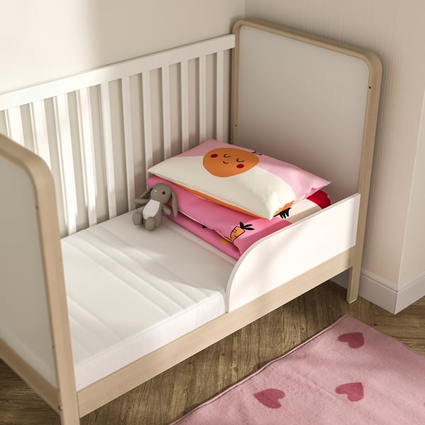 Cosy baby bed with JÄTTETRÖTT mattress. White frame, pink cushion, small rabbit toy. Soft hearts rug. Safe, comfy space for infants.