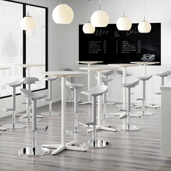 Modern café with high tables and white stools. Blackboard menu reads coffee & drinks. Light wooden floor, white pendant lamps overhead.