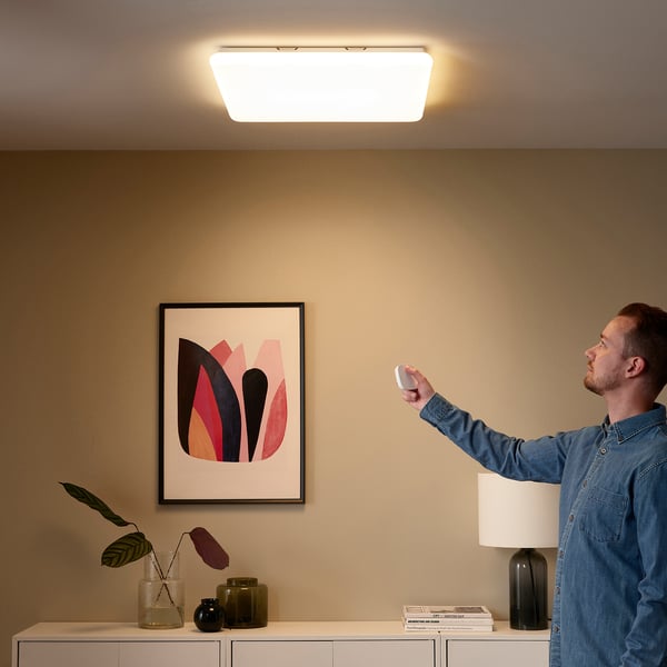 Person controls smart led light panel with remote, adjusting brightness and warmth.