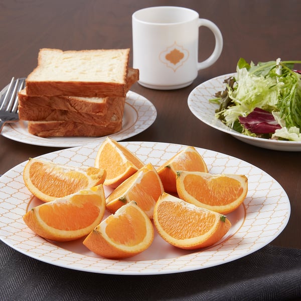 Breakfast setup: KALASBRA glass dishes with sliced oranges, toasted sandwiches, salad, and mug.