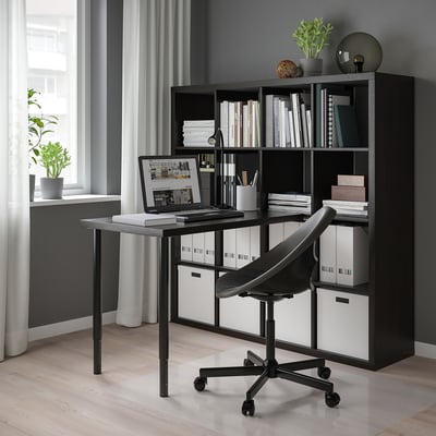 Home office with KALLAX shelf, desk, chair, laptop, books, plants, and window.