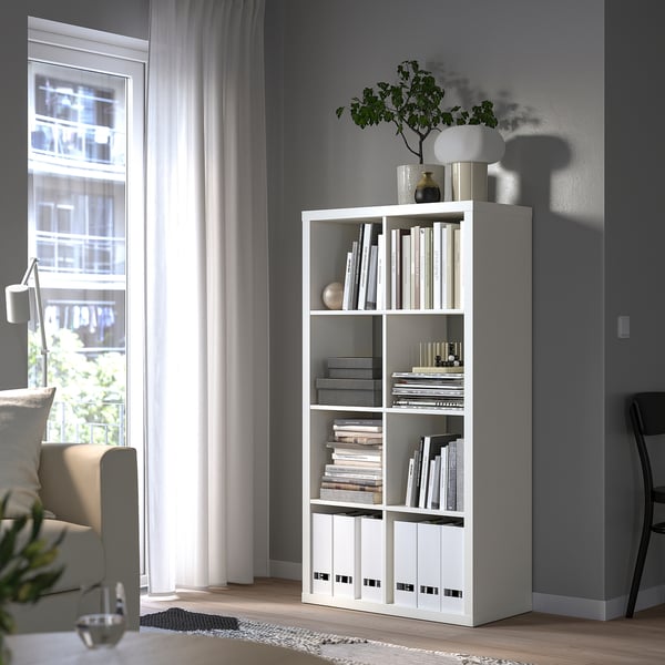 KALLAX shelving with books, lamp, plant beside window and chair.